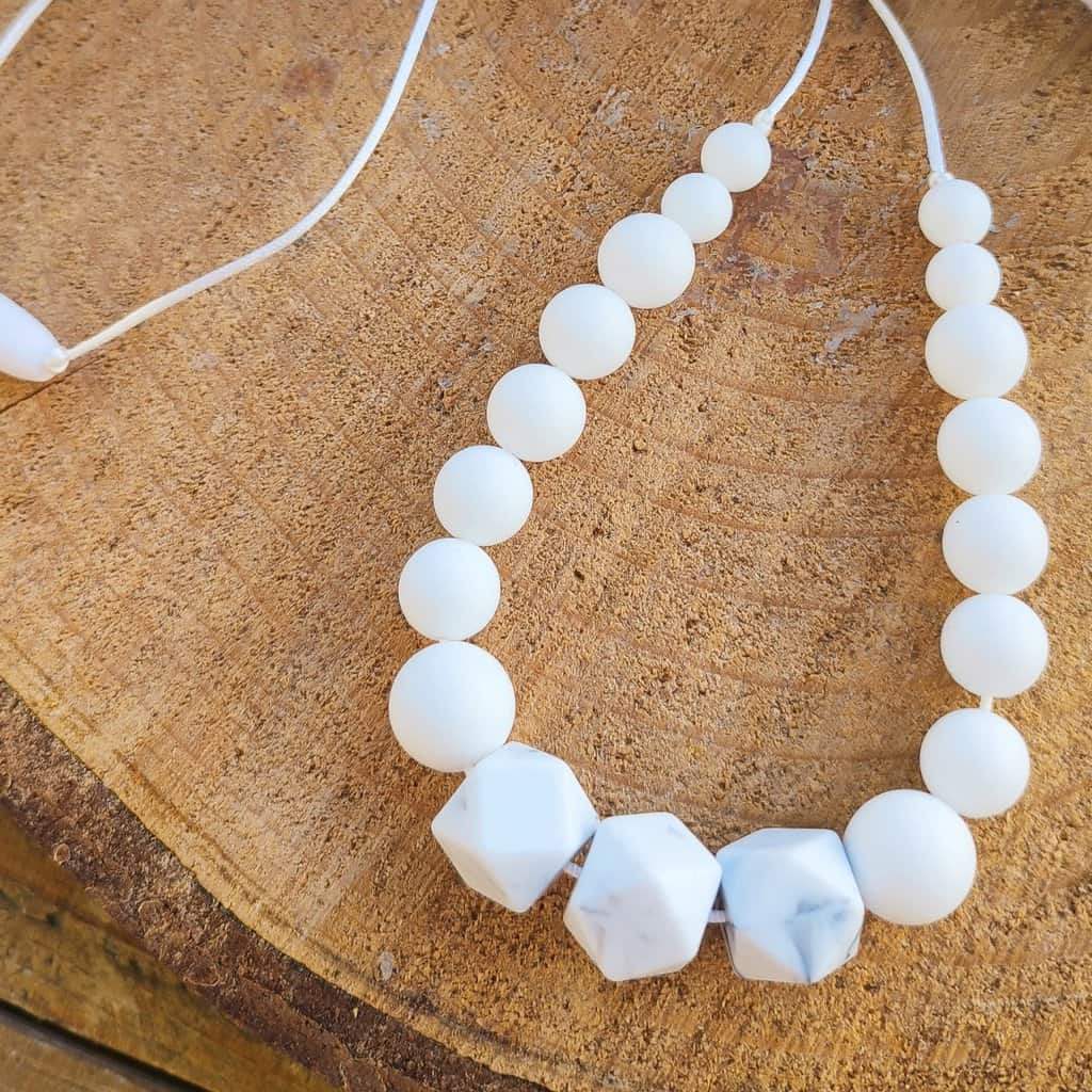 Collier d'allaitement Couleur blanc marbré avec un fond en bois, 4 petites perles en silicone alimentaire de 9 mm, 8 moyenne perles en 12 mm et 5 perles en 15 mm.