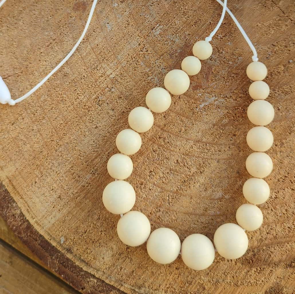 Collier d'allaitement Couleur crème avec un fond en bois, 4 petites perles en silicone alimentaire de 9 mm, 8 moyenne perles en 12 mm et 5 perles en 15 mm.